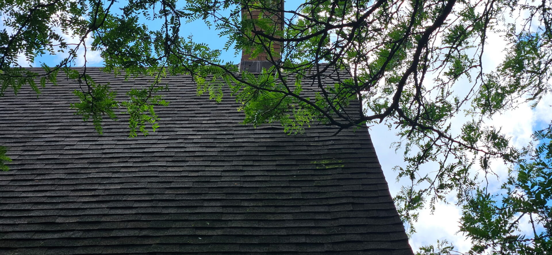 Close-up of new architectural asphalt shingles and the brick chimney on a Claremont A-frame cottage roof