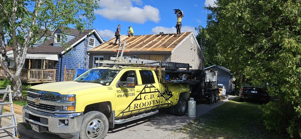 C.D. Roofing crew rebuilding the roof deck on an Ajax wartime home with the branded company truck parked in front