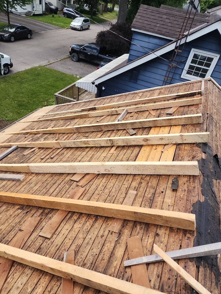 Stripped roof deck on an Ajax wartime home showing old board sheathing and the 5-inch structural sag, with new tapered rafters installed to rebuild it flat
