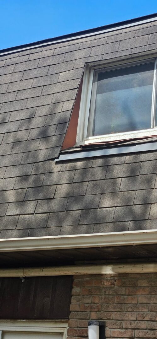 Roof window on a steep mansard slope in Ajax showing damaged sheet metal and worn asphalt shingles before repair