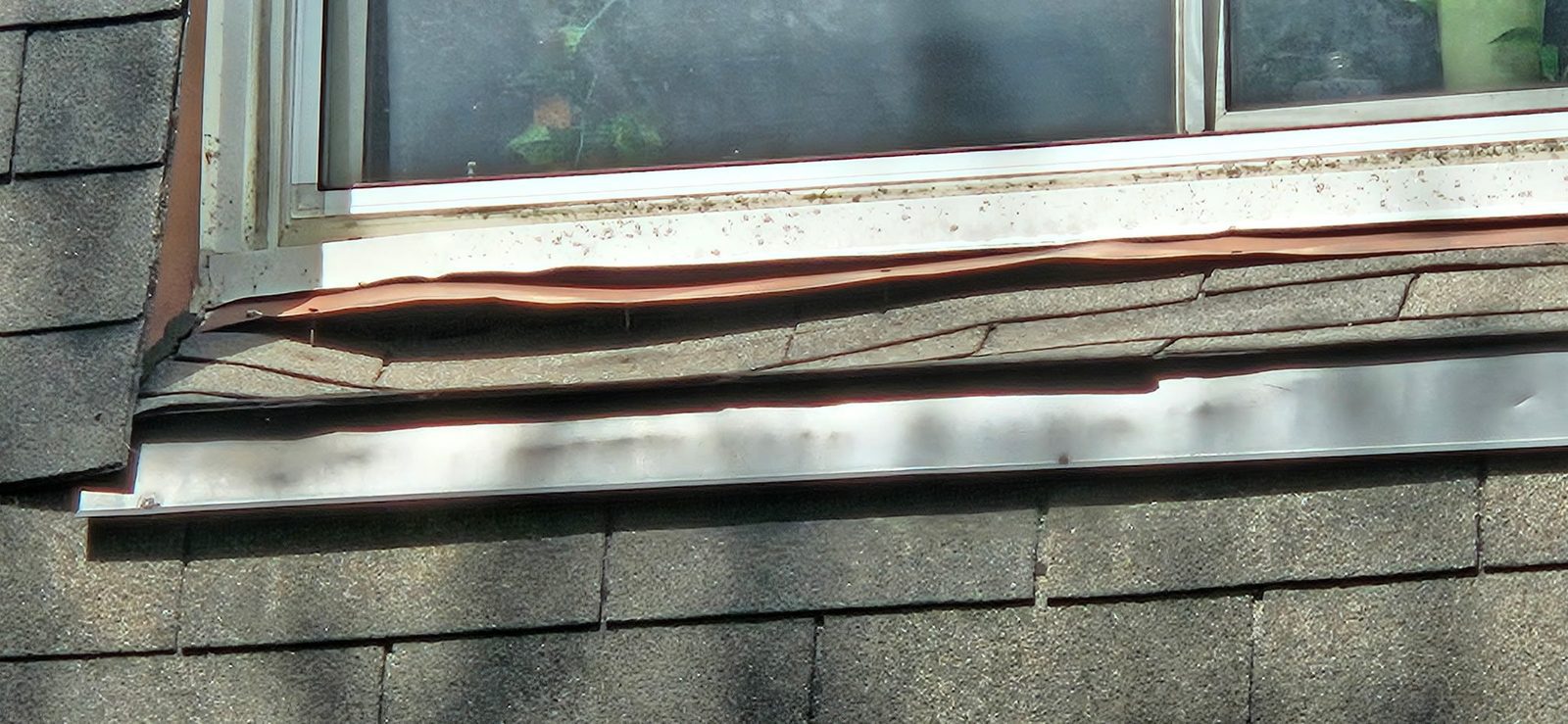 Close-up of buckled and lifted sheet metal flashing under a roof window sill in Ajax before repair